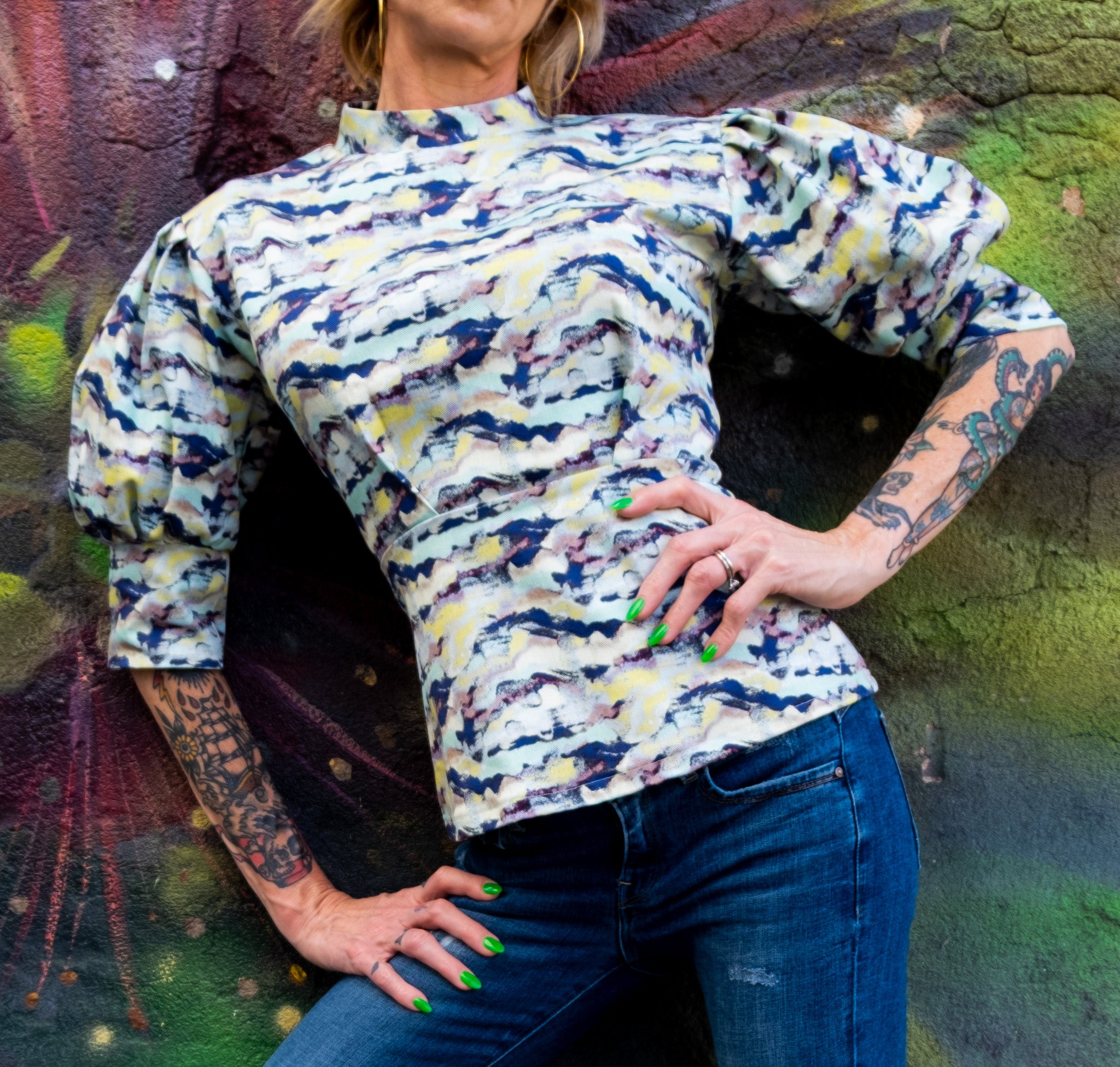 A close-up of a model with tattoos wearing a high-neck print top with jeans 